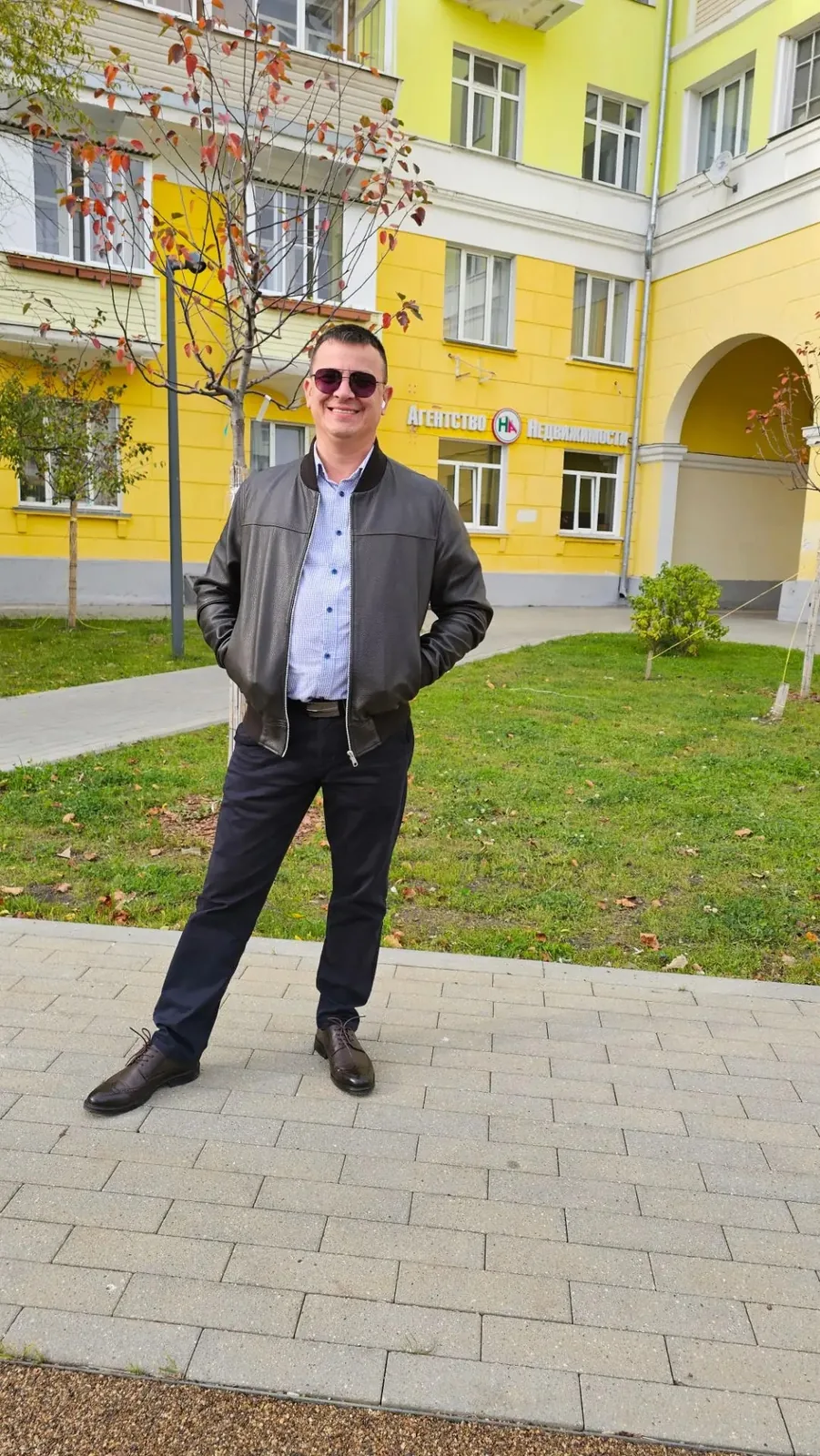 Максим Малышев, агент по недвижимости, у здания с вывеской «Агентство недвижимости»