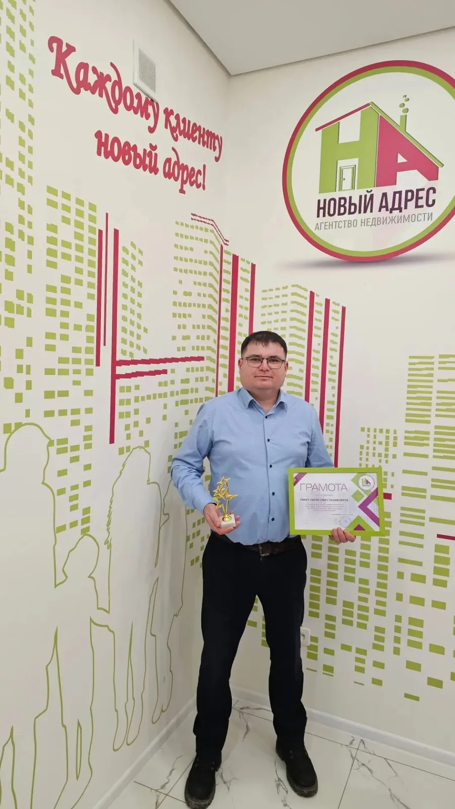 Ринат Галимзянов с грамотой и статуэткой агентства на фоне надписи «Каждому клиенту новый адрес!»